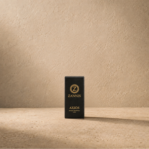 A black rectangular product box standing upright on a textured beige surface against a matching beige wall. The box has gold lettering that reads 'ZANNIS' and 'AXIOS' with a circular 'Z' logo above.