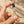 A hand holding a small clear glass perfume sample spray vial with a black atomizer cap. The vial features gold lettering that reads 'ZANNIS AXIOS'.