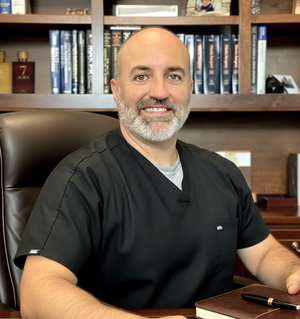 Man in black scrubs sitting in a chair with a bookshelf in the background